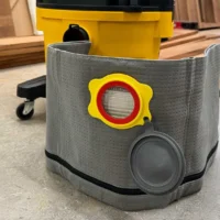 Macam reusable dust bag with gray polyester exterior, yellow plastic collar with red ring opening, and dark gray cap port, mounted on a Dewalt shop vac