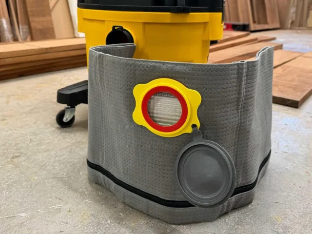 Macam reusable dust bag with gray polyester exterior, yellow plastic collar with red ring opening, and dark gray cap port, mounted on a Dewalt shop vac