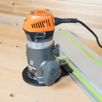 Black guide rail adapter base mounted under an orange Ridgid 2 HP fixed base router riding a track