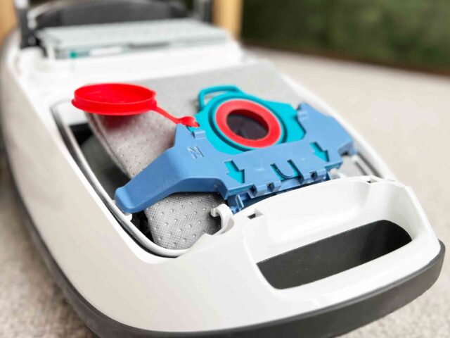 Blue and red reusable dust bag with microfleece filter insert sitting in white Miele vacuum canister