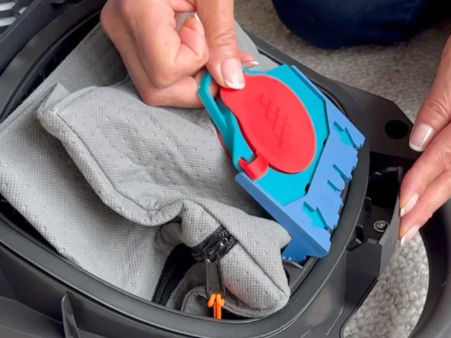 Macam reusable dust bag in blue and red, held in hand above an open Miele vacuum canister with gray fabric interior