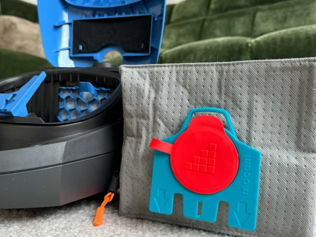 Macam reusable dust bag with red cap and grid pattern mounted on blue backing, displayed next to Miele vacuum