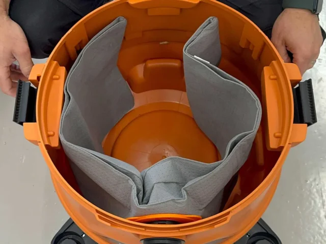 Orange dust bag with gray polyester interior and elastic opening, shown open and held by two hands, revealing inner chamber and rigid plastic base