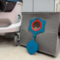 Blue Macam reusable dust bag with red ring opening, displayed in front of a gray fabric container next to a Makita dust extractor