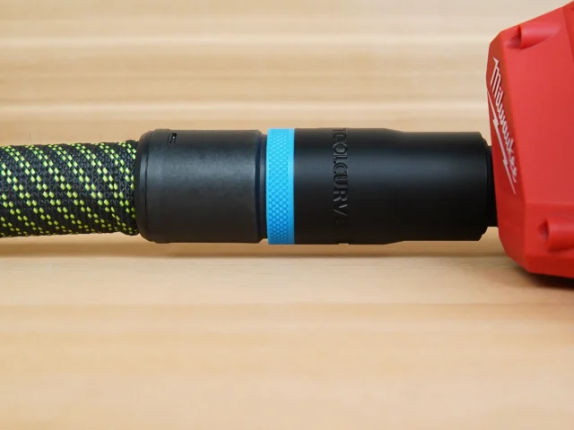 Black ToolCurve hose adapter with blue band attached to braided hose, connected to red Milwaukee planer port