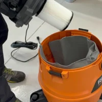 Orange Ridgid shop-vac with gray reusable dust bag installed inside, shown from above with power cord and filter cartridge visible nearby