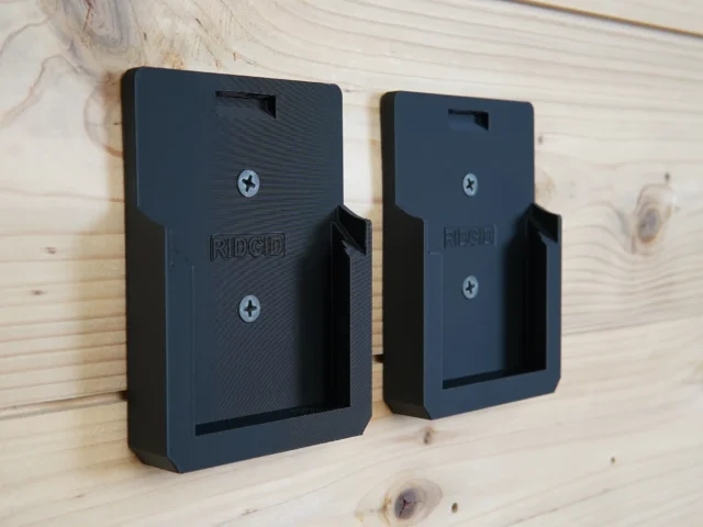 Two black plastic battery mounts labeled Ridgid mounted on a light wood wall, each with a rectangular opening and two screw holes