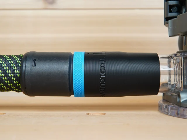 Black hose adapter with blue band installed on Ridgid router, braided hose attached to left end, clear connector on right