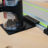 Black plastic guide rail adapter mounted on SKIL 20v trim router, positioned on a Festool track saw rail with bright green stripe