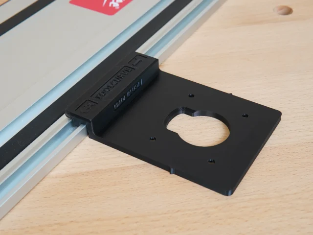 Black plastic guide rail adapter mounted on Festool track rail, with oval cutout for router base and mounting holes visible