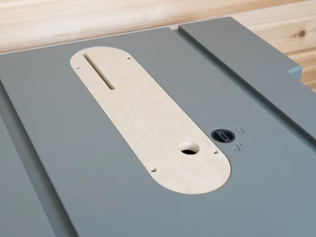 Cream-colored zero clearance insert for Hercules 10" table saw, installed on gray table saw top, showing central blade slot and mounting holes