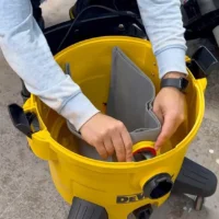 Macam reusable dust bag installed on yellow DeWalt shop vac, showing gray fabric interior and elastic top opening in use