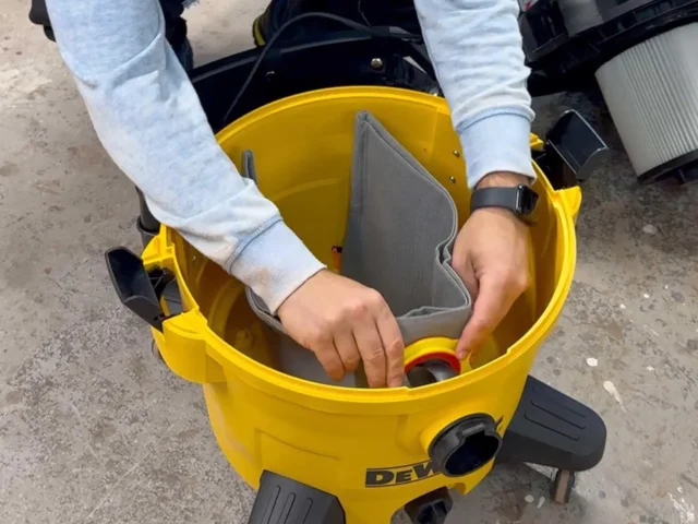 Macam reusable dust bag installed on yellow DeWalt shop vac, showing gray fabric interior and elastic top opening in use
