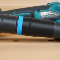 Black hose adapter with blue band attached to Makita grinding shroud, showing threaded connection and identification marking