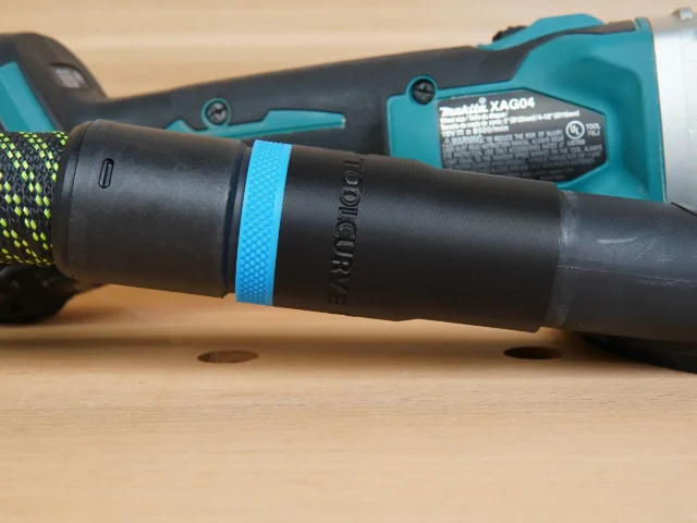 Black hose adapter with blue band attached to Makita grinding shroud, showing threaded connection and identification marking