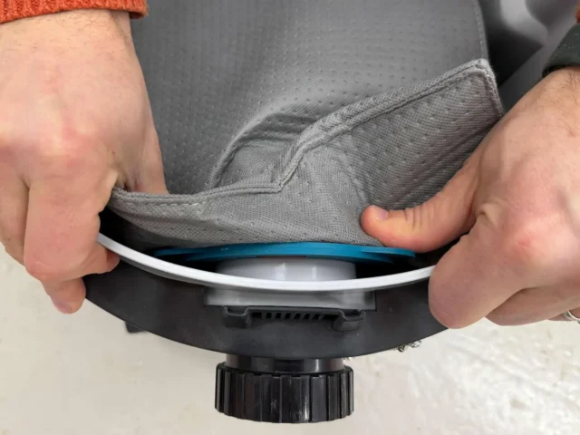 Gray reusable dust bag being installed on a Makita VC4210 dust extractor, with blue trim ring visible at the connection point