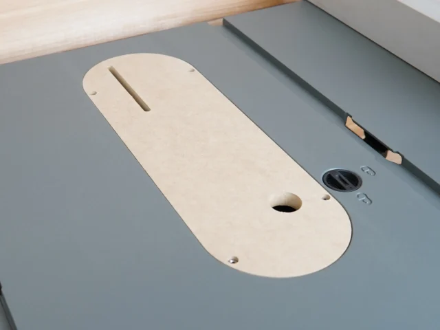 Cream-colored MDF zero clearance insert with slot and mounting holes, installed on a Craftsman table saw with gray top