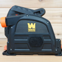 Side view of a black 6-1/2-inch track saw dust cover fitted to a WEN track saw on wood, showing the WEN logo and orange knob.