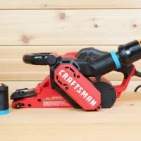 Black 1-1/4 inch ToolCurve hose adapter with blue band beside a Craftsman belt sander with hose attached