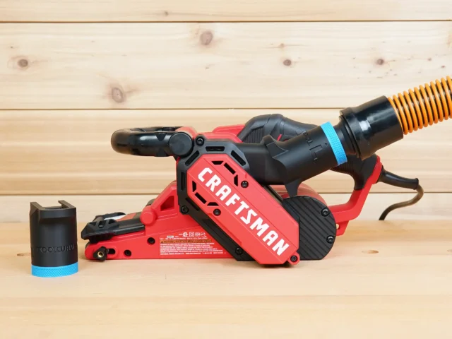 Black 1-1/4 inch ToolCurve hose adapter with blue band beside a Craftsman belt sander with hose attached