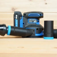 Black and blue ToolCurve 1-1/4" hose adapter joined to an orange vac hose beside a Kreg random orbit sander