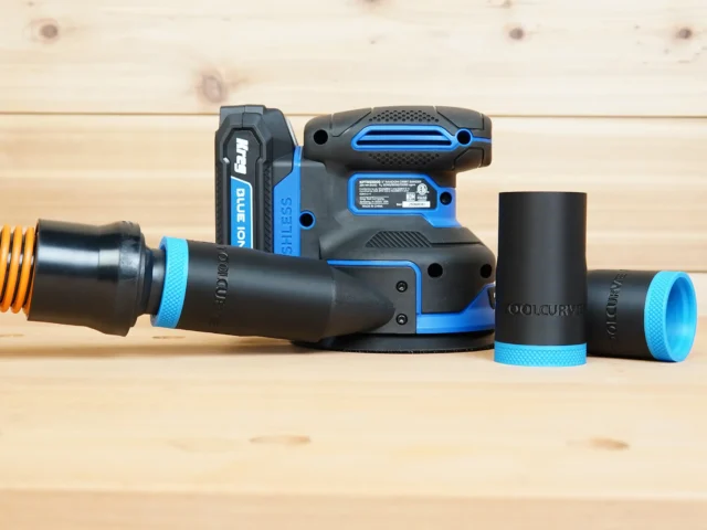 Black and blue ToolCurve 1-1/4" hose adapter joined to an orange vac hose beside a Kreg random orbit sander