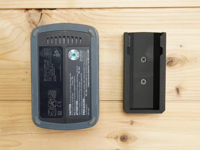 Black ToolCurve battery mount next to a Festool BP 18v battery, showing the mount's screw holes and slot for battery insertion