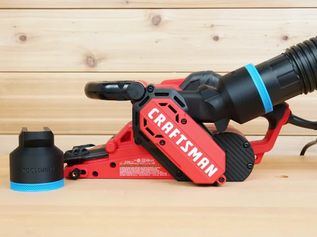 Black ToolCurve 2-1/2 inch hose adapter with blue band beside a Craftsman belt sander, second adapter on its dust port