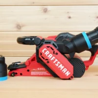 Black ToolCurve 1-7/8 inch hose adapter with blue band beside a Craftsman belt sander, second adapter installed on its rear dust port