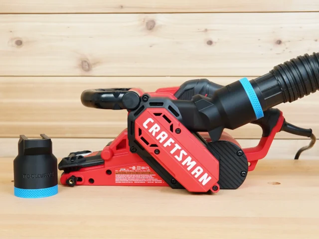 Black ToolCurve 1-7/8 inch hose adapter with blue band beside a Craftsman belt sander, second adapter installed on its rear dust port