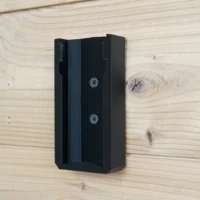 Black plastic battery mount screwed to wooden wall surface with two visible fasteners, open slot facing forward ready to receive a Festool BP 18v battery