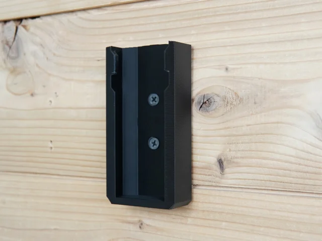 Black plastic battery mount screwed to wooden wall surface with two visible fasteners, open slot facing forward ready to receive a Festool BP 18v battery