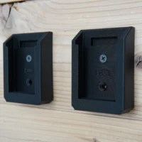 Two black plastic battery mounts for SKIL 20v PWRCORE batteries mounted on light wood, each with a Phillips screw hole and mounting port