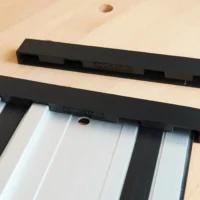Two black protective caps for PowerTec guide rails, one installed on an aluminum rail with friction-fit slots visible, one shown separately