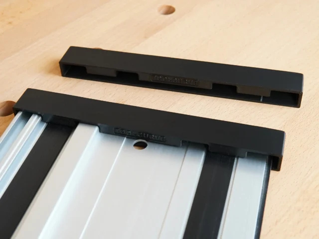 Two black protective caps for PowerTec guide rails, one installed on an aluminum rail with friction-fit slots visible, one shown separately