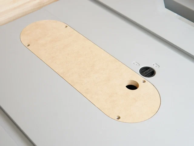 Light tan MDF zero clearance insert for Kobalt 10-inch table saw, with one oval cutout and mounting holes, set in a white table saw throat