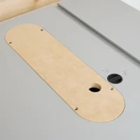 Tan MDF zero clearance insert with rounded ends, center slot, and mounting holes, positioned on a gray table saw top