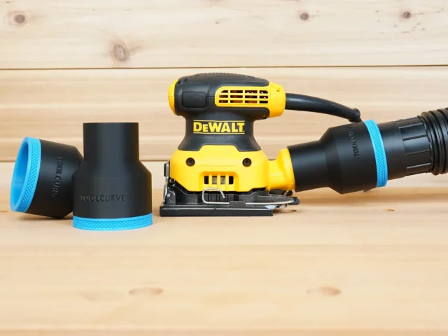 Black ToolCurve 2-1/2 inch hose adapter with blue trim installed on a DeWalt palm sander, second adapter beside it