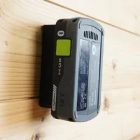 Black plastic battery mount with green button holding a Festool 18V LiPowerMill battery against a wooden wall