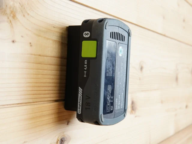 Black plastic battery mount with green button holding a Festool 18V LiPowerMill battery against a wooden wall