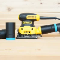 Black ToolCurve hose adapter with blue ring installed on a DeWalt palm sander dust port, two spares beside it
