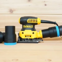 Black ToolCurve 36mm hose adapter with blue ring joining a vacuum hose to a DeWalt palm sander, spare adapters beside