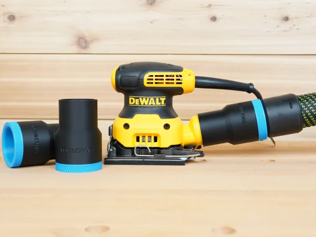 Black ToolCurve 36mm hose adapter with blue ring joining a vacuum hose to a DeWalt palm sander, spare adapters beside