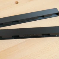 Two black PETG protective caps for PowerTec guide rails, shown separately on a wooden surface with dowel holes visible