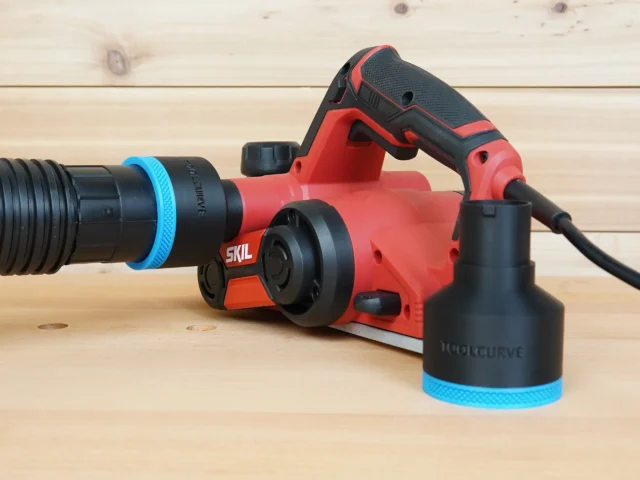 Black ToolCurve 2-1/2 inch hose adapter with blue trim on a red SKIL planer port, second adapter beside it