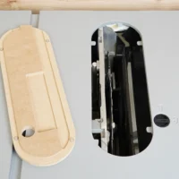 Cream-colored MDF zero clearance insert shown front and back, with mounting holes and rounded ends, next to black metal insert assembly for Kobalt 10″ table saw.
