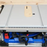 Zero clearance insert in light wood mounted on Kobalt table saw, showing slot for blade and adjustment holes