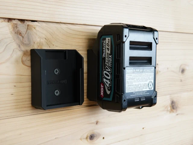 Black plastic battery mount holder installed on wood wall next to a Makita 40v Max XGT battery
