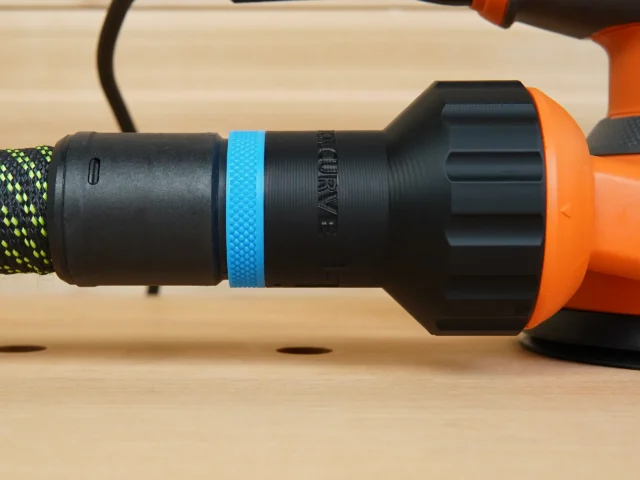 Black plastic hose adapter with blue grip band attached to Ridgid 5-inch sander's rear dust port, orange tool body visible