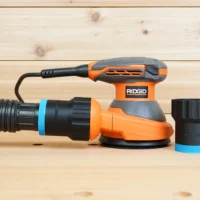 Black ToolCurve 1-7/8 inch hose adapter with blue band joining a vacuum hose to a Ridgid 5 in. sander, second adapter beside it